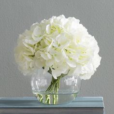 a clear vase with white flowers on top of a blue tableclothed bookcase