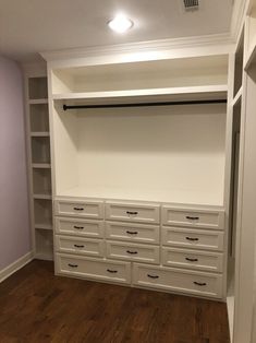 an empty walk in closet with white cabinets and drawers on the bottom shelf, along with dark wood flooring