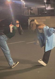 two people on skateboards doing tricks in an empty parking lot with one person holding a drink