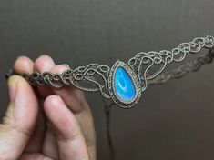 a hand holding a silver chain with a blue stone on it