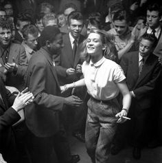 black and white photograph of woman dancing with man in suit, crowd looking at her