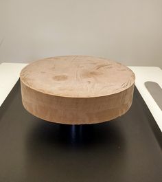 a round wooden object sitting on top of a black table next to a white wall