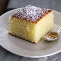 a piece of cake on a white plate with a spoon in it and powdered sugar on top