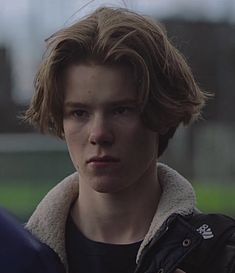 a young man with brown hair and a black jacket is looking at something in the distance