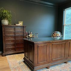 a large wooden desk sitting in front of a window next to a dresser and chair