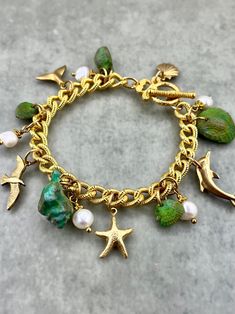 WHAT IT IS: A "Seaside Soirée" theme charm bracelet featuring hand-painted vintage lucite seashells, vintage solid brass charms, and freshwater pearls, all dangling from a 10k gold plated chain with a toggle clasp.  THE SPECS: - 7.5 inches total length. - Toggle clasp closure. WHY IT'S SPECIAL: The vintage lucite seashells began in subtle hues of white, tan, and coral. While lovely as they were, we meticulously hand-painted them in various layers to add depth and playful, colorful charm. With the transformed, vibrant shells hung from an elegant gold-plated chain and adorned with  genuine freshwater pearls, this "Seaside Soirée" bracelet balances colorful whimsy with tasteful sophistication--capturing the lively essence of a coastal celebration. This bracelet comes in purple too! Take a loo Artisan Jewelry Handmade, Brass Charms, Vintage Lucite, Toggle Clasp, Gold Plated Chains, Handmade Artisan, Charm Bracelets, 10k Gold, Czech Glass