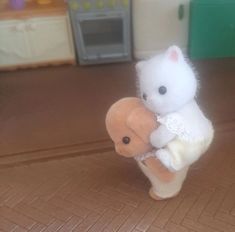 a small white stuffed animal holding an orange teddy bear on a brown floor next to a microwave oven