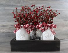 two mason jar vases with red berries tied around the top, sitting on a wooden box