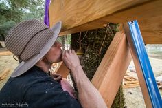 a man in a hat is working on a wooden structure with blue tape around it