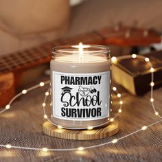 a candle that reads pharmacy school survivor on it next to some string lights and a guitar