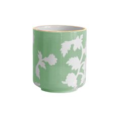 a green and white cup with leaves on the outside, sitting in front of a white background