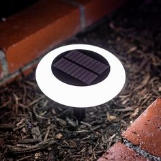 a solar powered light on the ground in front of a red brick wall at night