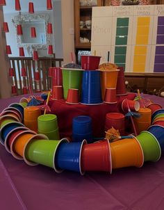 there are many cups in the center of this colorful tablecloth on top of a purple table cloth