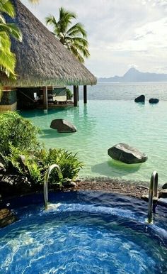 a hot tub in the middle of some water with rocks and palm trees around it