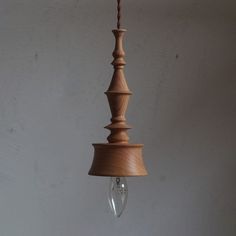 a wooden light hanging from a ceiling with a white wall behind it and a small glass droplet in the middle