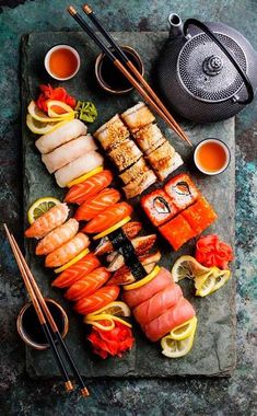 an assortment of sushi on a stone platter with chopsticks and tea