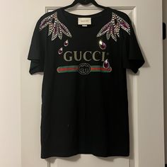 Gucci Print Tee With Embellishment Along The Neckline/Shoulder Area. Tee Shirt Is Size Xs, But Fits Like Size M/Size 6. Worn Twice, In Brand New Condition. Luxury Gucci Graphic Tee, Gucci Short Sleeve T-shirt, Luxury Gucci Short Sleeve T-shirt, Gucci Print, Gucci Black T-shirt With Logo Print, Gucci Cotton Graphic Print T-shirt, Gucci Top, Print Tee, Printed Tees