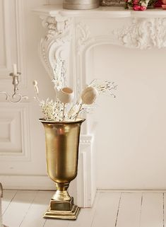 a gold vase with flowers in it sitting on a white floor next to a fireplace