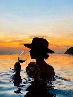 a person in the water with a glass of wine and a hat on their head