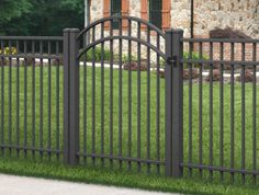 an iron fence in front of a stone building with green grass and trees behind it