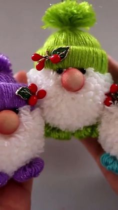 two small knitted santa claus ornaments are being held by someone's hand with green and purple hair