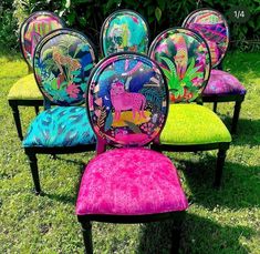 four colorful chairs sitting in the grass with different designs on them and one has a pink seat