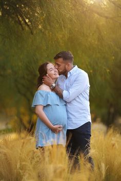 a pregnant couple cuddles in tall grass as the sun shines down on them