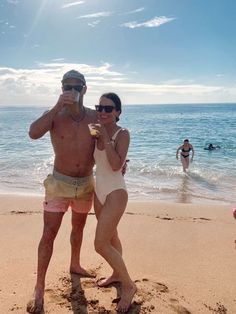 a man and woman standing on the beach drinking beverages