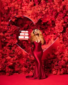 a woman standing in front of a red wall with roses and a heart shaped box