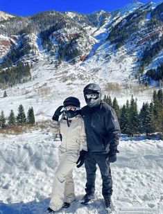 two snowboarders pose for a photo in front of a snowy mountainside area