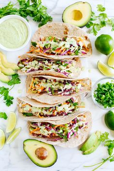 several tortillas with coleslaw, carrots and avocado on the side