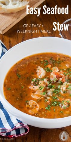 a white bowl filled with seafood stew on top of a wooden table next to bread