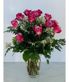 a vase filled with lots of pink roses on top of a white countertop next to greenery