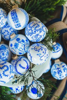 blue and white ornaments are arranged in a basket with pine branches on the table top