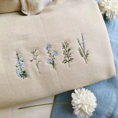 some flowers are sitting on the table next to an embroidered bag and two white daisies