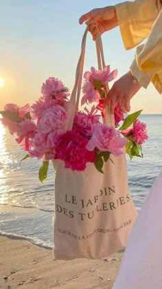 a person holding a bag with flowers in it on the beach near the ocean at sunset