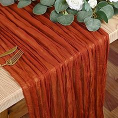 an orange table runner with white flowers and greenery on the top, along with a gold utensil