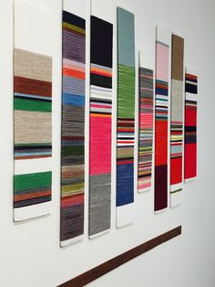 a group of colorful rugs hanging on a white wall next to a wooden shelf