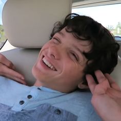 a young boy smiles while sitting in the back seat of a car with his hand on his ear