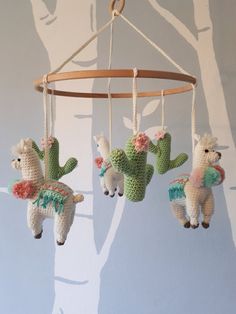 three crocheted llamas hanging from a tree branch with flowers on them