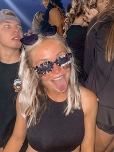 a woman with her tongue out and some people in the background wearing sunglasses on top of her head