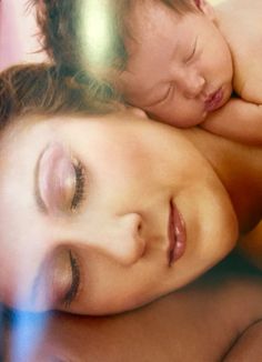 a woman and child laying next to each other on top of a bed with their eyes closed