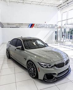 a silver bmw car parked in a showroom with white tile flooring and large windows