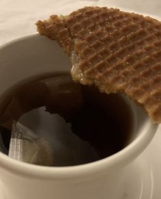 a waffle sandwich with syrup in a white cup on a saucer next to a spoon