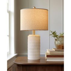 a white table lamp sitting on top of a wooden table next to a book shelf