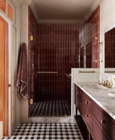 a bathroom with black and white checkered floor, red cabinetry, and gold fixtures