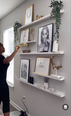 a woman standing in front of a wall with pictures and plants on it's shelves