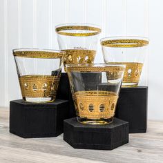 four glass cups sitting on top of a black stand with gold trimming around them