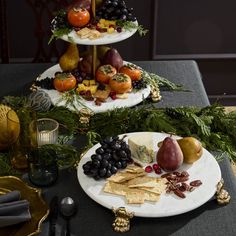 two plates topped with fruit and crackers on top of a table covered in greenery