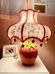 a strawberry lamp sitting on top of a white table next to a small photo frame